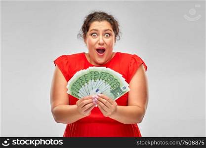 people and finances concept - surprised woman in red dress holding hundreds of euro money banknotes over grey background. shocked woman holding hundreds of money banknotes