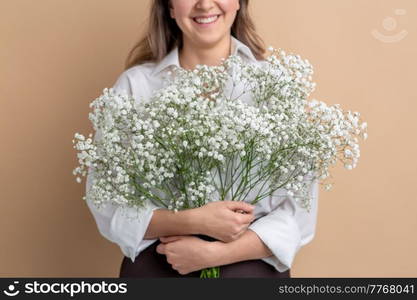 people and floral design concept - close up of happy smiling woman holding bunch of gypsophila flowers over beige background. portrait of smiling woman holding bunch of flowers