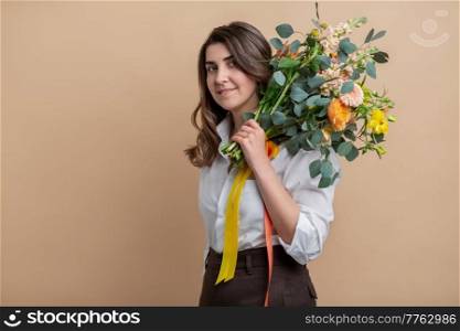 people and floral design concept - portrait of happy smiling woman holding bunch of flowers over beige background. portrait of happy woman holding bunch of flowers