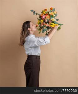 people and floral design concept - portrait of happy smiling woman holding and smelling bunch of flowers over beige background. portrait of happy woman smelling bunch of flowers