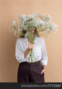 people and floral design concept - portrait of woman holding bunch of gypsophila flowers over beige background. portrait of woman holding bunch of flowers