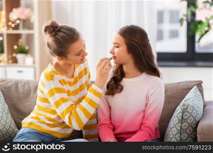 people and friendship concept - happy teenage girls sitting on sofa and doing make up at home. happy teenage girls doing make up at home
