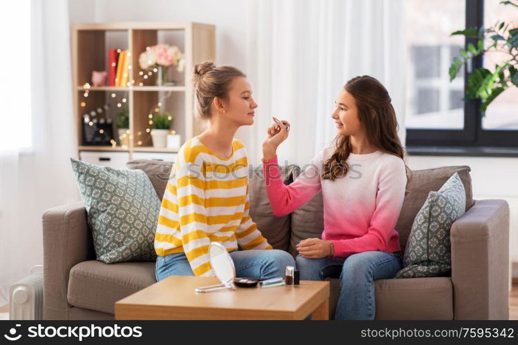 people and friendship concept - happy teenage girls sitting on sofa and doing make up at home. happy teenage girls doing make up at home