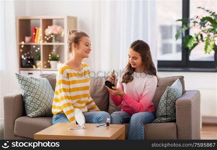 people and friendship concept - happy teenage girls sitting on sofa and doing make up at home. happy teenage girls doing make up at home