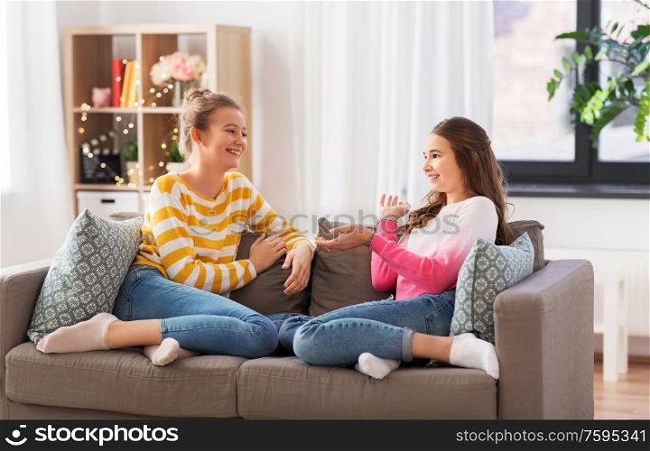 people and friendship concept - happy teenage girls sitting on sofa and talking at home. happy teenage girls talking on sofa at home