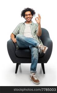 people and furniture concept - happy smiling young man in glasses sitting in chair and showing ok gesture over white background. happy man sitting in chair and showing ok gesture