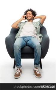 people and furniture concept - happy smiling young man in glasses sitting in chair and calling on smartphone over white background. smiling man sitting in chair calling on smartphone