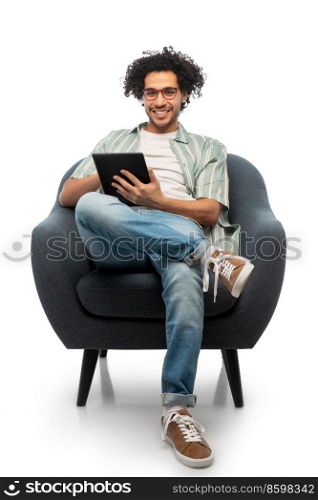 people and furniture concept - happy smiling young man in glasses with tablet pc computer sitting in chair over white background. smiling young man with tablet pc sitting in chair