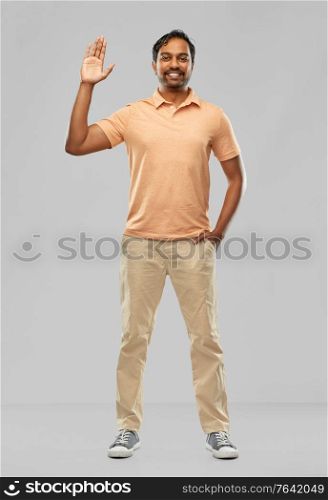 people and furniture concept - portrait of happy smiling young indian man waving hand over grey background. portrait of happy smiling young indian man