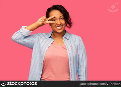 people and gesture concept - happy african american young woman showing peace hand sign over pink background. happy african american woman showing peace