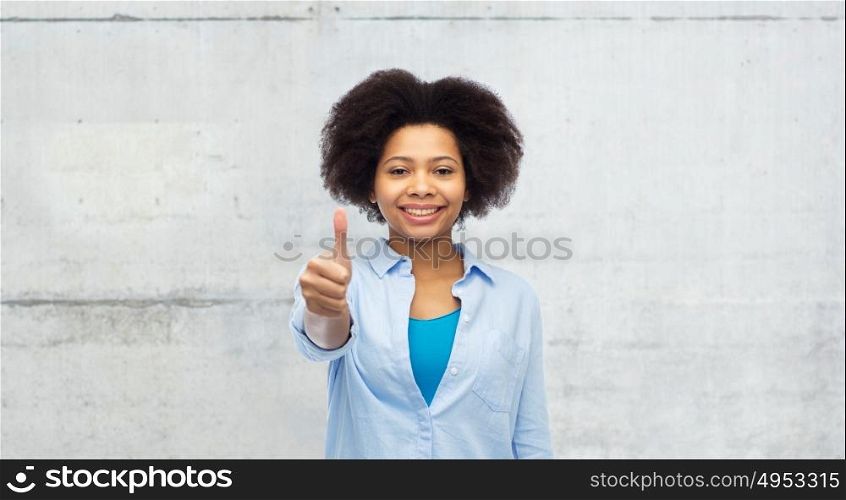 people and gesture concept - happy afro american young woman showing thumbs up over gray concrete wall background. happy afro american woman showing thumbs up