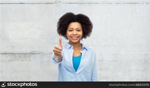 people and gesture concept - happy afro american young woman showing thumbs up over gray concrete wall background. happy afro american woman showing thumbs up