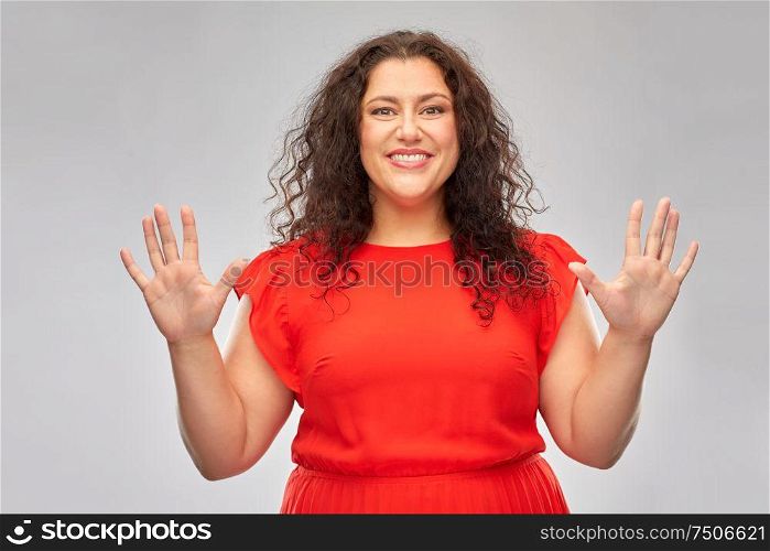 people and gesture concept - happy woman in red dress showing hand palms over grey background. happy woman in red dress showing hand palms