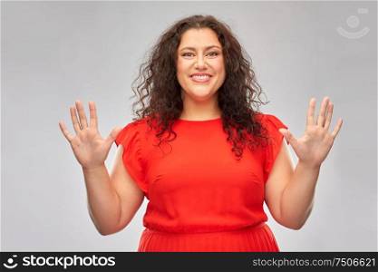people and gesture concept - happy woman in red dress showing hand palms over grey background. happy woman in red dress showing hand palms