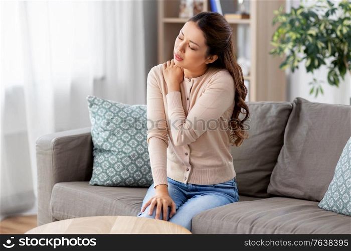 people and health problem concept - unhappy asian woman suffering from pain in in shoulder at home. asian woman suffering from shoulder pain at home