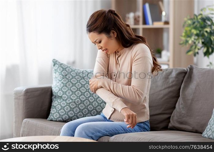 people and health problem concept - unhappy asian woman suffering from pain in hand at home. asian woman suffering from ache in hand at home