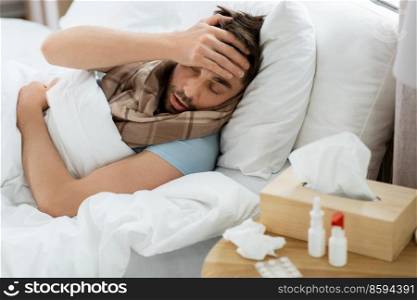 people and health problem concept - unhappy sick man having headache lying in bed at home. sick man having headache lying in bed at home