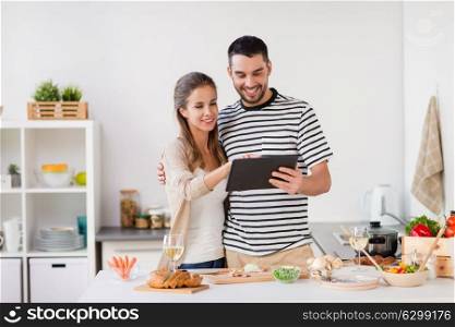 people and healthy eating concept - happy couple with tablet pc computer cooking food at home kitchen. happy couple with tablet pc cooking food at home