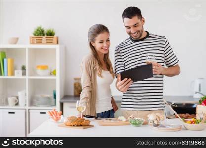 people and healthy eating concept - happy couple with tablet pc computer and non alcoholic wine cooking food at home kitchen. happy couple with tablet pc cooking food at home