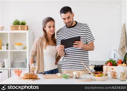 people and healthy eating concept - happy couple with tablet pc computer cooking food at home kitchen. happy couple with tablet pc cooking food at home