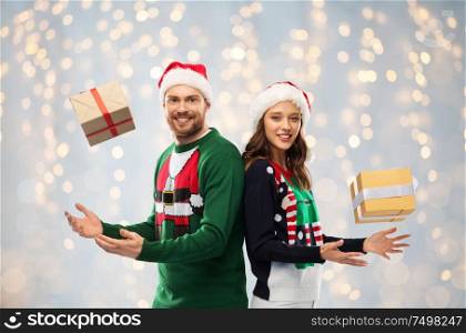 people and holidays concept - happy couple in santa hats with christmas gifts at ugly sweater party over festive lights background. happy couple in sweaters with christmas gifts