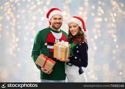 people and holidays concept - happy couple in santa hats with christmas gifts at ugly sweater party over festive lights background. happy couple in sweaters with christmas gifts
