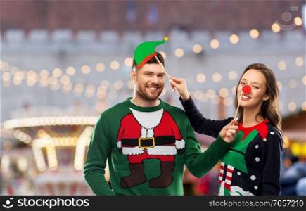 people and holidays concept - happy couple in sweaters posing with party props over christmas market background. couple in sweaters with christmas party props
