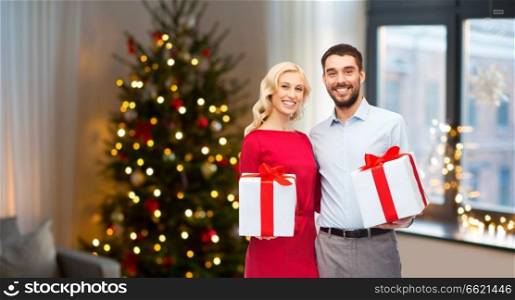 people and holidays concept - happy couple with gift boxes over home room and christmas tree background. happy couple with christmas gifts at home