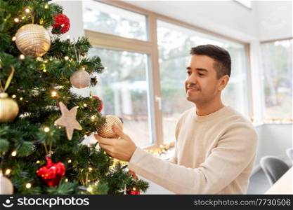 people and holidays concept - happy smiling middle aged man decorating christmas tree at home. happy middle aged man decorating christmas tree