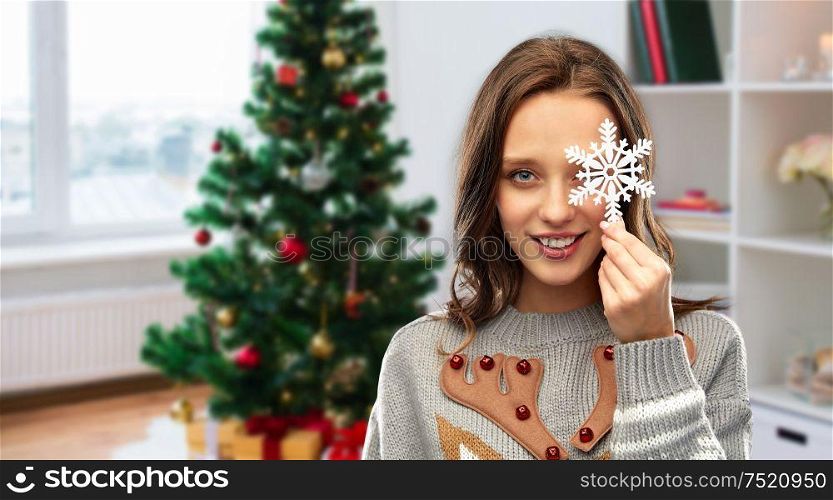 people and holidays concept - happy young woman with snowflake decoration wearing ugly sweater over christmas tree on home background. woman in christmas sweater with snowflake at home