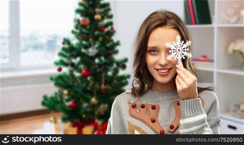 people and holidays concept - happy young woman with snowflake decoration wearing ugly sweater over christmas tree on home background. woman in christmas sweater with snowflake at home