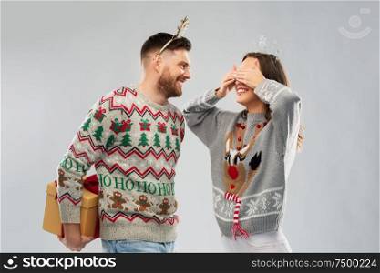 people and holidays concept - portrait of happy couple with christmas gift at ugly sweater party. happy couple in christmas sweaters with gift box