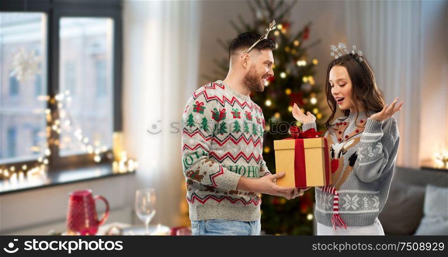 people and holidays concept - portrait of happy couple with christmas gift at ugly sweater party. happy couple in christmas sweaters with gift box