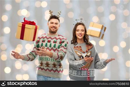 people and holidays concept - portrait of happy couple with christmas gifts at ugly sweater party over festive lights background. happy couple in christmas sweaters with gift boxes