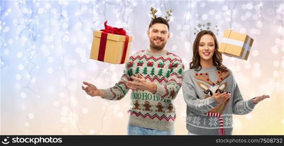 people and holidays concept - portrait of happy couple with christmas gifts at ugly sweater party over festive lights background. happy couple in christmas sweaters with gift boxes