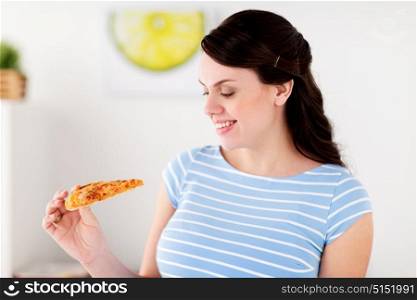 people and junk food concept - happy woman eating pizza at home kitchen. happy woman eating pizza at home kitchen
