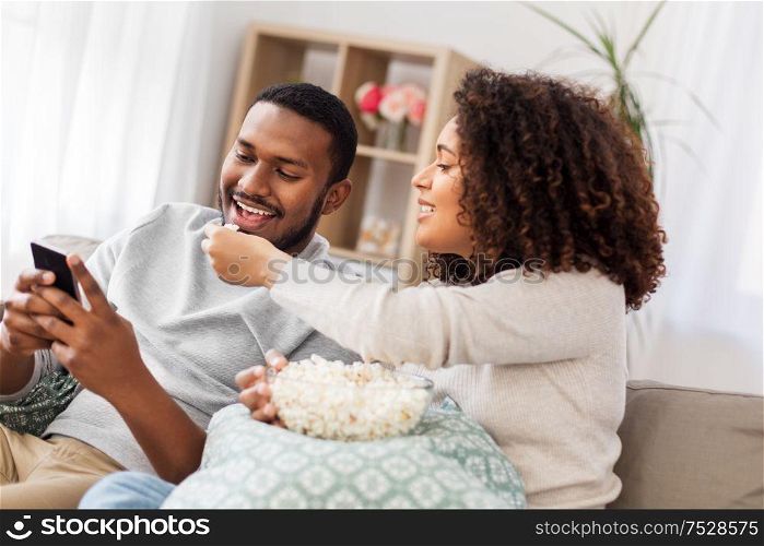 people and leisure concept - african american couple with popcorn and smartphone at home. african couple with popcorn and smartphone at home