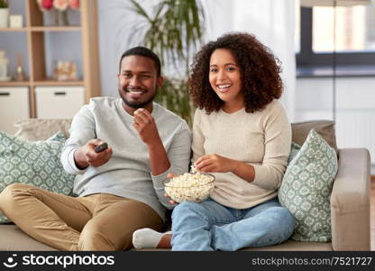 people and leisure concept - african american couple with popcorn watching tv at home. african couple with popcorn watching tv at home