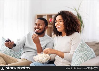 people and leisure concept - african american couple with popcorn watching tv at home. african couple with popcorn watching tv at home