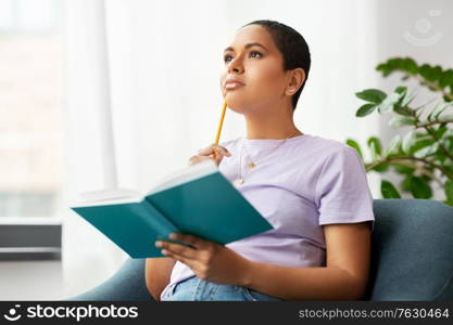 people and leisure concept - african american woman with diary and pencil sitting in chair at home. african american woman with diary at home