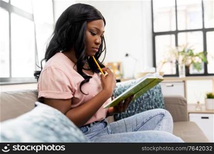 people and leisure concept - african american woman with diary and pencil sitting in chair at home. african american woman with diary at home