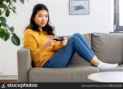 people and leisure concept - asian young woman with gamepad playing video game at home. asian woman with gamepad playing game at home
