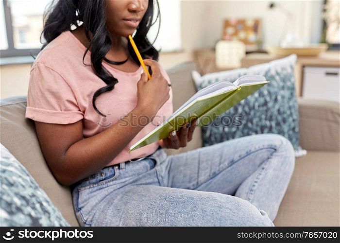 people and leisure concept - close up of african american woman with diary and pencil sitting in chair at home. african american woman with diary at home