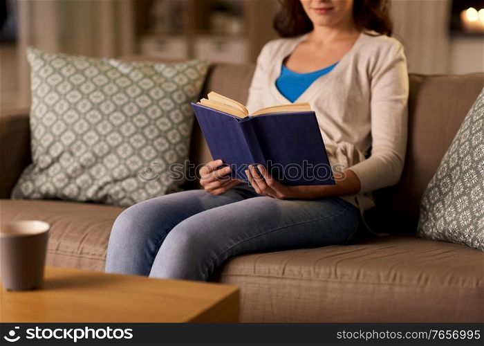 people and leisure concept - close up of young woman sitting on sofa and reading book at home. close up of young woman reading book at home