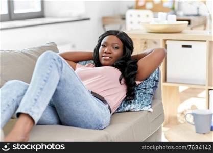 people and leisure concept - happy african american young woman lying on sofa at home. happy african american young woman at home
