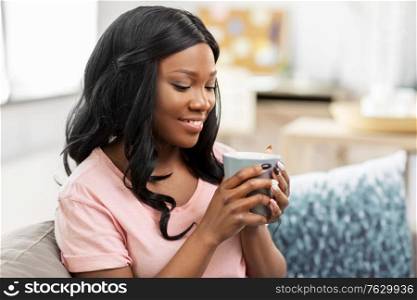 people and leisure concept - happy smiling african american woman drinking tea or coffee at home. happy african woman drinking tea or coffee at home