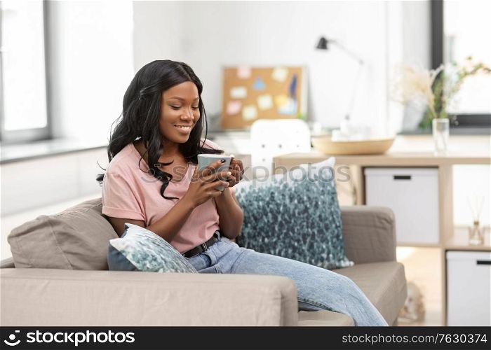 people and leisure concept - happy smiling african american woman drinking tea or coffee at home. happy african woman drinking tea or coffee at home