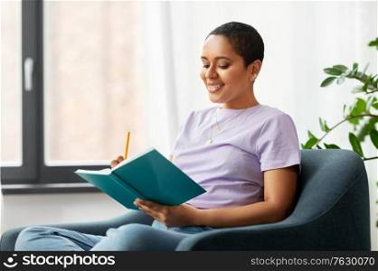 people and leisure concept - happy smiling african american woman with diary sitting in chair at home. happy african american woman with diary at home