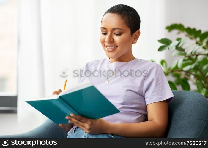 people and leisure concept - happy smiling african american woman with diary sitting in chair at home. happy african american woman with diary at home