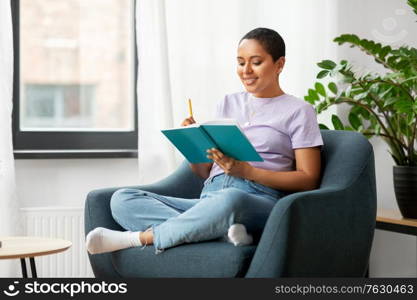 people and leisure concept - happy smiling african american woman with diary sitting in chair at home. happy african american woman with diary at home